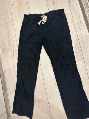 Svarta linnebyxor från Roxy - Snygga svarta linnebyxor från Roxy med avslappnad passform och dragsko i midjan av rep. Byxorna har två fickor fram och är perfekta för en chill och bekväm stil. Tillverkade i lätt och luftigt linnematerial.