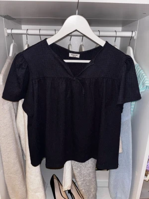 Marinblå blus med kort ärm och knyt - Snygg marinblå blus med korta ärmar och ett litet knyt framtill vid halsen. Blusen har en lös passform och lätt struktur i tyget, perfekt till jeans eller kjol. Enkel men trendig design som passar till många olika stilar.