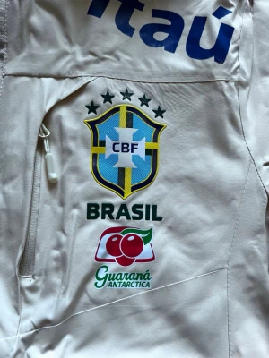 Beige Brasilien Windbreaker  - Beige Brasilien Windbreaker i storlek M, Den är i perfekt skick och har aldrig användas. Suverän kvalitet och perfekt för fotbollsälskare som vill vara redo inför kommande årstider