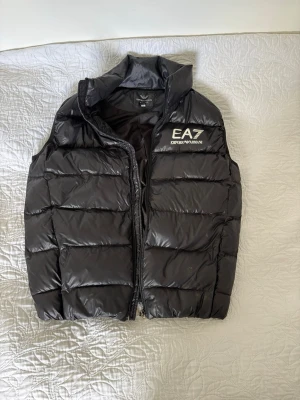 Svart dunväst från Emporio Armani - Säljer min Emporio Armani EA7 väst då den inte kommer till användning nån mer. Storlek L, passar även M i storleken. Pris kan diskuteras.