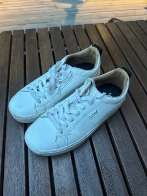 Vita låga sneakers från björnborg - Stilrena vita sneakers från björnborg  i lågt snitt. Skorna har klassisk snörning, ovandel i slätt läder och diskret logga på sidan. Insidan är beige och sulan är vit. Perfekta för en clean och enkel look.