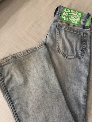 Ljusblå jeans från Cheap Monday - Säljer ett par ljusblå jeans från Cheap Monday med klassisk femficksdesign och coolt grönt märke bak i midjan. Jeansen har bootcut ben och är tillverkade i bomull med lite elastan för extra stretch. Perfekta för en avslappnad och trendig look.