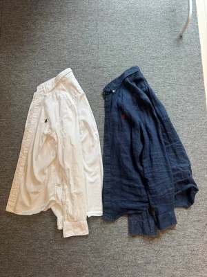 Ralph lauren skjorta i vit och marin blå  - Säljer en vit Ralph lauren skjorta i vanligt skjort material och en marin blå linne skjorta från Ralph lauren, till ett riktigt bra bundle pris. Båda skjortorna är i storlek xs om man jämför med vuxen storlek.