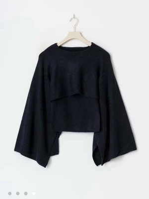 Svart poncholiknande stickad tröja - Säljer en svart stickad tröja med vid, poncholiknande passform och vida ärmar. Tröjan har en unik asymmetrisk design med kortare framstycke och längre sidor.