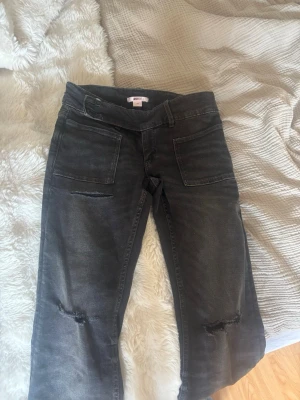 Svarta raka jeans med slitningar - Säljer ett par svarta jeans med raka ben och slitningar vid knäna. Jeansen har stora framfickor och klassiska bakfickor. Materialet är denim med en tvättad look som ger en cool och avslappnad stil. Perfekta till sneakers eller boots.