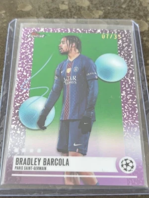 Bradley Barcola PSG topps chrome - Unikt samlarkort från Topps med Bradley Barcola i Paris Saint-Germain. Kortet har lila och gröna detaljer, två blå bollar och är numrerat 07/33. Perfekt för dig som gillar fotboll och samlar på Champions League-relaterade kort.