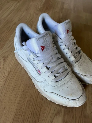 Vita Reebok Classic sneakers - Säljer ett par vita Reebok Classic sneakers i mocka. Använda men går lätt o tvätta i tvättmaskin så ser dom ut som nya igen!