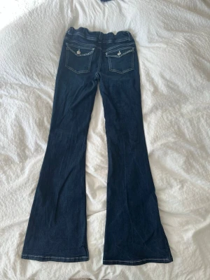 Mörkblå bootcut jeans med fickdetaljer - Säljer ett par mörkblå bootcut jeans med detaljer på fickorna, dom är från Ryvls.