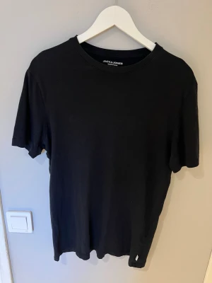 Svart t-shirt från Jack & Jones - En  svart t-shirt från Jack & Jones med rund hals och korta ärmar. Tillverkad i mjuk bomull för skön passform. Perfekt till jeans eller shorts för en clean och stilren look. Passar även perfekt att ha under en tröja.