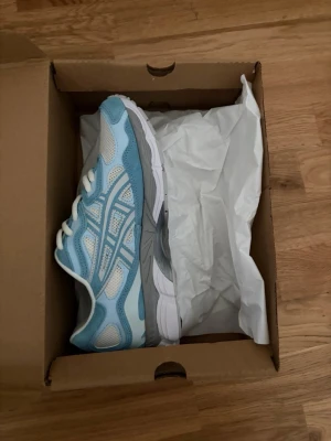 Blåvita sneakers med meshdetaljer - Snygga sneakers från Asics i ljusblått, storlek 44 självklart ingår box. inte används i överhuvudtaget pågrund av att dom satt dåligt på mig och gick ej att skicka tillbaka drf säljs dom nu!