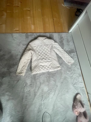 Ljusbeige quiltad trenchcoat - Snygg ljusbeige trenchcoat med quiltat mönster och klassisk krage. Jackan har raka ärmar och är fodrad på insidan för extra komfort. Passar perfekt till lager på lager och ger en stilren look till din outfit.