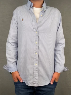 Ralph lauren skjorta vit/blå randig M - Säljer denna magiskt fräscha ralph lauren skjorta. Riktigt skönt material . Size 15 1/2 som motsvarar M. Modellen är 180cm. Bredd 50cm,  längd 72cm! Fint skick, nytvättad och ny strykt så att skillnaden på denna och en ny ska vara minimal! Tyvärr har en knapp lossnat, går att sätta dit lätt om man vill! Fraktar samma dag som köp, kan gå ner i pris vid snabb affär! 🤩