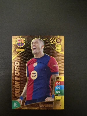 Panin Raphinha Balón de Oro samlarkort - Säljer ett Panini Raphinha Balón de Oro samlarkort med en FC Barcelona-tröja. Kortet har guldfärgad bakgrund och detaljer, samt färgade siffror och klubbmärke. Perfekt för dig som samlar på fotbollskort eller gillar Raphinha