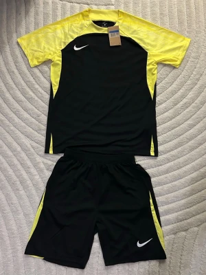 Nike svart och gul träningsset - Gul och svart träningsset från Nike. Storlek M, helt ny och oanvänd. Perfekt nu under sommar och för träning. Fraktas inom 24 timmar efter köp📦🚛