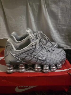 Nike Shox silver sneakers - Snygga Nike Shox sneakers i helsilver med futuristisk design och ikoniska fjädrande sulor. Ovandelen är i mesh och syntetmaterial för bra andningsförmåga och komfort. Perfekta för dig som vill sticka ut med en unik och sportig look.