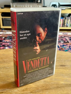 Inplastad och oanvänd VHS Vendetta (1995) - Ett unikt tillfälle för samlaren! Helt ny och fabriksinplastad svensk original-VHS av Jan Guillous actionklassiker Vendetta (1995) från Moviola. Stefan Sauk gör här sin ikoniska och hyllade tolkning av agent Carl Hamilton i ett stenhårt maffiadrama på Sicilien.  * Skick: Helt ny / Oöppnad (Fabriksinplastad med originalplasten intakt)  * Format: VHS (Köpfilm)  * Utgåva: Moviola / TV4 AB / Svensk Filmindustri  * Skådespelare: Stefan Sauk, Marika Lagercrantz, Erland Josephson, Mats Långbacka  Ovanl