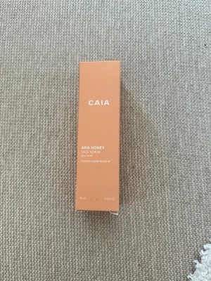 CAIA AHA Honey Face Scrub 75 ml - Säljer en CAIA AHA Honey Face Scrub i en snygg persikofärgad förpackning. Ansiktsskrubben innehåller AHA och honungsextrakt och kommer i en praktisk tub på 75 ml. Perfekt för dig som vill ha len och fräsch hud. Oöppnad och oanvänd, förpackningen är plomberad