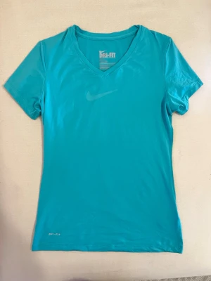 Tränings tröja  - Snygg turkos träningströja från Nike med Dri-Fit-teknologi som håller dig torr under träningspasset. T-shirten har V-ringning, korta ärmar och en diskret Nike-logga på bröstet. Perfekt för gymmet eller löprundan.