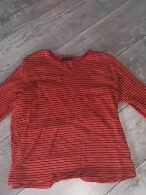 Randig röd topp från Exlindexlind - Säljer en randig topp från Exlindexlind i rött och orange med smala svarta ränder. Köpt second hand men har inga synliga tecken av användning!!