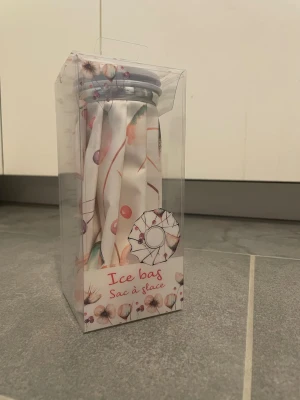 Is-påse med blommigt mönster - Säljer en is-påse i tyg med blommigt mönster i vitt, rosa och lila. Perfekt att fylla med is och använda på ömma eller skadade områden. Kommer i genomskinlig förpackning och har skruvlock i plast.