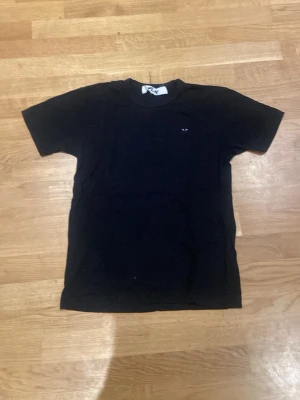 Svart t-shirt från Comme des Garçons - Svart t-shirt från Comme des Garçons Play i klassisk modell. T-shirten är kortärmad och har en liten logga på bröstet. Tillverkad i mjuk bomull som känns skön mot huden. Perfekt för en clean och stilren look. Är medium men sitter som en small.