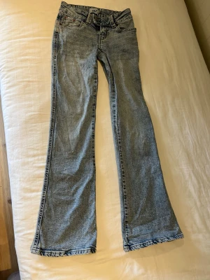 Ljusblå bootcut jeans med brodyr - Säljer ett par ljusblå bootcut jeans med snygg broderad detalj på bakfickan. Jeansen har klassisk femficksdesign, normal midja och är tillverkade i denim. Perfekta för dig som gillar en avslappnad men trendig look.