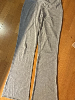 Grå mjukisbyxor med utsvängda ben - Säljer ett par ljusgrå mjukisbyxor med utsvängda ben. Byxorna har en hög midja som kan vikas ner och är gjorda i ett mjukt, stretchigt material som känns skönt mot huden. Perfekta för chill dagar hemma eller när du vill ha en avslappnad look.