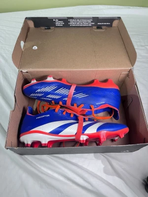 Adidas Predators - Säljer ett par Adidas Predator League FT FG fotbollsskor i blått, rött och vitt. Skorna har röda dobbar och snörning samt vita detaljer på sidan. Perfekta för spel på fasta underlag och ger grym kontroll på planen. Passar även st 41