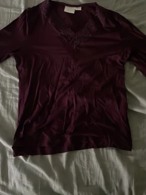 Vinröd topp med spets från Gina Tricot - Vinröd långärmad topp från Gina Tricot med v-ringning och dekorativ spetsdetalj vid halsen. Toppens material känns mjukt och har en elegant look, perfekt för dig som gillar stilrena plagg med en twist.
