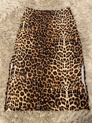 Leopardmönstrad långkjol i sammet - Säljer en snygg långkjol med leopardmönster i bruna och svarta toner. Kjolen har en rak passform och är gjord i mjuk sammet som ger en lyxig känsla. Perfekt för dig som vill sticka ut med ett djuriskt print.