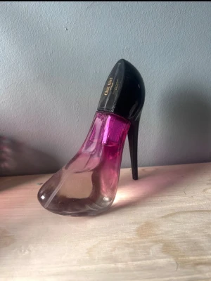Parfymflaska i form av högklackad sko - Unik parfymflaska formad som en högklackad sko med svart häl och lock samt rosa och transparent glas. Flaskan har en modern och trendig design som sticker ut på sminkbordet. Perfekt för dig som gillar snygga detaljer och vill ha något annorlunda i din parfymkollektion.