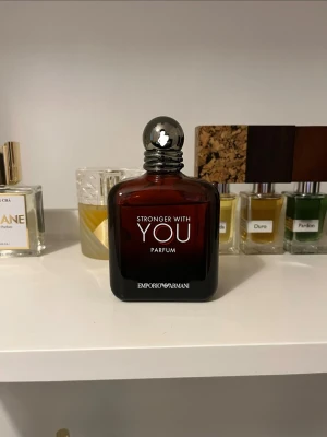 Stronger With You Parfum 100 ml - Stronger With You Parfum från Emporio Armani i en elegant mörkröd glasflaska med rundad form och silverfärgad kork. Doften kommer i en stilren svart kartong med röda detaljer. Flaskan rymmer 100 ml och har en modern, lyxig känsla.