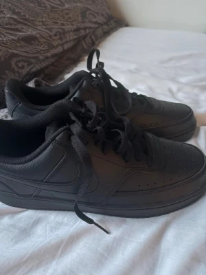 Helsvarta låga sneakers i läder - Snygga helsvarta sneakers med lågt skaft och klassisk siluett. Skorna har ovandel i slätt läder, svarta skosnören och diskreta sömmar. Perfekta för en clean och stilren look till vardags. Ventilationshål på tån för extra komfort.
