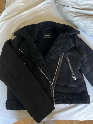 Svart teddyjacka från Stradivarius XS - PRIA GÅR ATT DISKUTERA! Snygg svart teddyjacka från Stradivarius i storlek XS. Jackan har stora dragkedjor, bred krage och mysigt teddyfoder. Perfekt för kalla dagar med sin trendiga bikerstil och detaljer i silver. Materialet är mjukt och fluffigt, vilket ger en cool look.