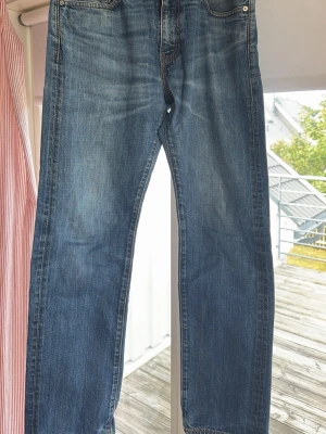 Levis  jeans med slitningar - Säljer ett par klassiska blå jeans med raka ben och snygga slitningar. Jeansen har fem fickor och normal midja. Materialet är denim i bomull och färgen är en tvättad blå nyans med ljusare partier framtill och baktill.