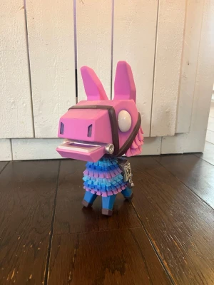 Funko pop Fortnite llama - Säljer en stor funko pop Fortnite llama i plast med färgerna rosa, blå och lila. Figurerna har en kantig, tecknad design och detaljer som sadel och sadelväska. Perfekt för dig som gillar gaming och vill ha coola spelprylar i hyllan.