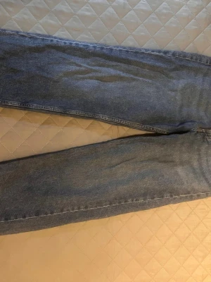 Blå raka jeans i klassisk modell - Säljer ett par blå jeans med rak passform och hög midja. Jeansen har klassiska bakfickor och är gjorda i ett slitstarkt denimtyg. Perfekta för dig som gillar en tidlös och enkel stil.