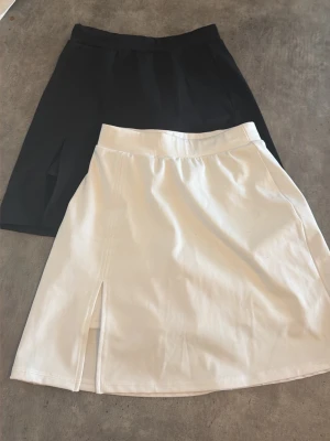 HM SPORT Svart och vit kortkjol med slits - Två stilrena kjolar i svart och vitt, båda i kort modell med slits framtill. Kjolarna har en enkel och clean design med bred linning och är perfekta för en trendig vardagslook. Materialet känns mjukt och följsamt. Inbyggda shorts 