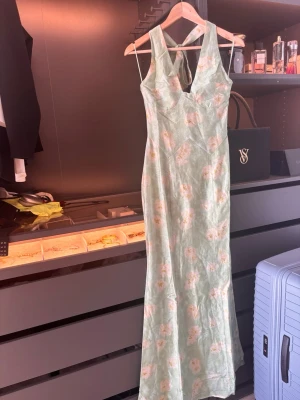 Adoora- Halter Dress Pastel Green  - Säljer en ljusgrön långklänning med blommigt mönster. Klänningen har v-ringad hals och en feminin passform.  Helt ny med prislappen på. 