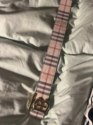 Rutig beige och rosa bälte med guldspänne - Ett bälte från burberry med guld B märke. Går att göra både svart och den klassiska burberry färgen. Bra för allt och fin bälte. Pris kan diskutera privat 