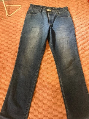 Blå raka jeans med broderad ficka - Snygga blå jeans med rak passform och klassisk femficksdesign. Jeansen har en broderad detalj på ena bakfickan med ett blommotiv. Tillverkade i denim med lätt tvättad look och bälteshällor i midjan.