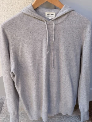 Ljusgrå Kashmir hoodie från Soft Goat - Mysig ljusgrå hoodie från Soft Goat i mjuk kashmir. Klassisk modell med huva och dragsko, samt ribbade muddar vid ärmslut och nederkant. Perfekt för en chill och avslappnad stil. Passar dig som gillar premiumkänsla och enkel design. Den är använd och har ett hål i ena axeln men som lätt kan sys ihop hemma eller hos skräddare 