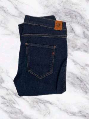 Replay Jeans Hyperflex Mörkblå - Snygga mörkblå jeans från Replay med klassisk femficksdesign och kontrastsömmar. Jeansen sitter hyfsat tajt men perfekt för dig som har denna storlek. Perfekta till vardags och lätta att matcha med olika outfits. W27 L30