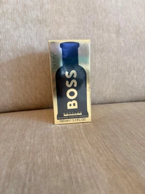 Hugo Boss Bottled Parfym 100 ml - Hugo Boss Bottled parfym i en lyxig guldfärgad förpackning med svart flaskmotiv. Flaskan rymmer 100 ml och har en modern, stilren design som känns exklusiv. Perfekt för dig som gillar klassiska och eleganta dofter.