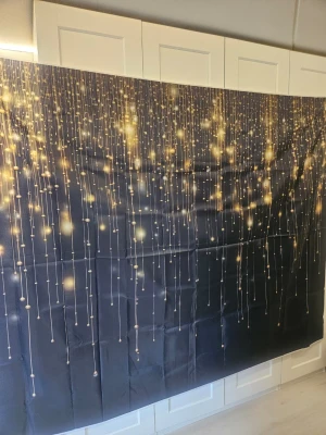 Svart fotovägg i tyg med guldmönster - Säljer ett stort svart tygstycke med tryck av hängande guldglittrande ljuspunkter och linjer. Perfekt som bakgrund till fest, fotografering eller dekoration. Materialet är tunt och lätt att hänga upp. Måtten är 230x180 cm