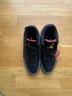 Svarta sneakers med färgglad sula - Säljer ett par svarta sneakers med gulddetaljer och färgglad sula i rött, gult och blått. Skorna har klassiskt elefantmönster runt tån och hälen samt svart läderöverdel. Insidan är svart med röd kant. Perfekta för dig som gillar streetwear och unika detaljer.