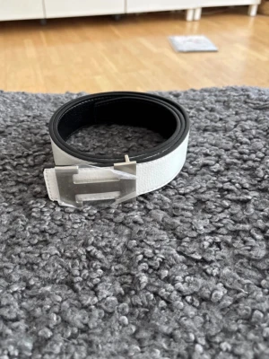 Svart och vitt skärp med metallspänne - Snyggt skärp i svart och vitt med ett stort metallspänne framtill. Skärpet har en stilren design och är tillverkat i skinn med en slät yta på utsidan och präglad insida. Perfekt accessoar för att lyfta din outfit. Går att ändra till svart och vitt 
