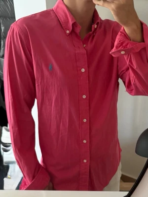 Rosa skjorta med knappar - Säljer en stilren och klassisk skjorta från Ralph Lauren. Perfekt för både vardag och mer uppklädda tillfällen.  Storlek: L Passform: slim fit Färg: Rosa Skick: Mycket bra  Skjortan är tillverkad i högkvalitativt material och har den ikoniska Ralph Lauren-loggan broderad på bröstet.  Hör av dig vid intresse eller frågor!
