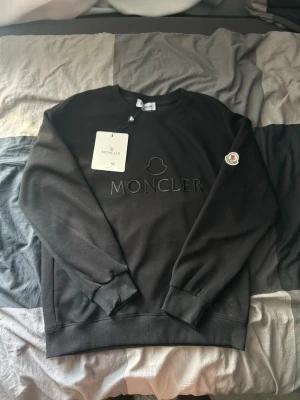 Moncler tröja  - Snygg svart sweatshirt från Moncler med broderad logga på bröstet och Moncler-märke på ärmen. Tröjan har rund halsringning, ribbade muddar och är gjord i mjukt bomullsmaterial. Perfekt för en clean och stilren look.
