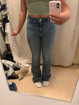 Blå bootcut jeans med hög midja - Säljer ett par klassiska blå bootcut jeans med hög midja och femficksmodell. Jeansen har en snygg tvätt och raka ben som går ut lite nedtill. Stängs med knapp och dragkedja. Perfekta till en crop top eller hoodie.